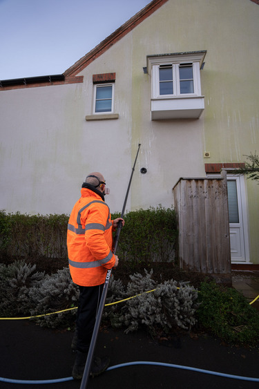 Stardust Cleaning operative in hi-vis applying professional soft wash treatment to algae-stained K-Rend render using extending pole equipment